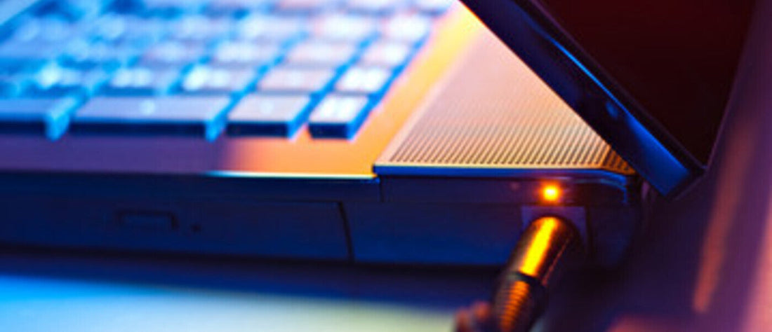 A close-up of a laptop with a power cable plugged in, illuminated with a soft glow.