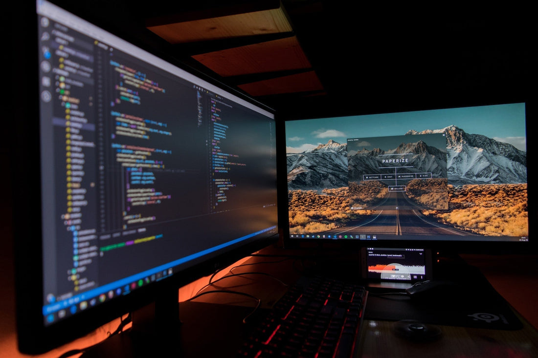 Dual monitor setup with one displaying coding and the other showing a scenic mountain road.