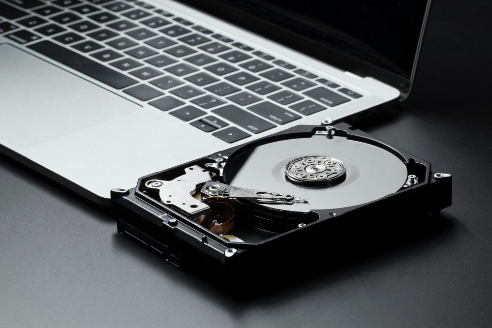 A close-up of an open hard drive placed next to a laptop, with visible internal components of the drive.