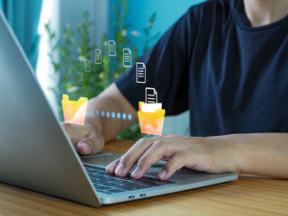 A person typing on a laptop with digital file icons appearing to be transferred or organized.