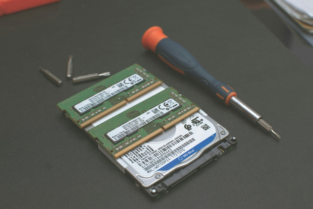 A screwdriver, screws, two RAM sticks, and a hard drive placed on a black surface, likely for computer repair or assembly.