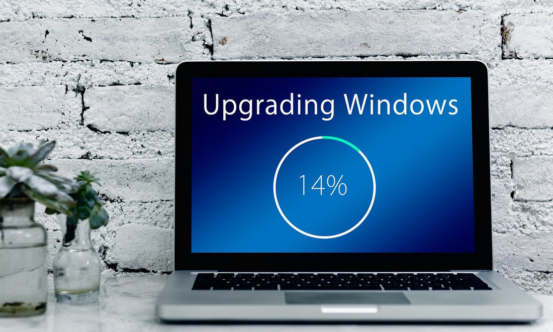 A laptop with a screen showing a progress bar at 14%, labeled Upgrading Windows, against a brick wall background.