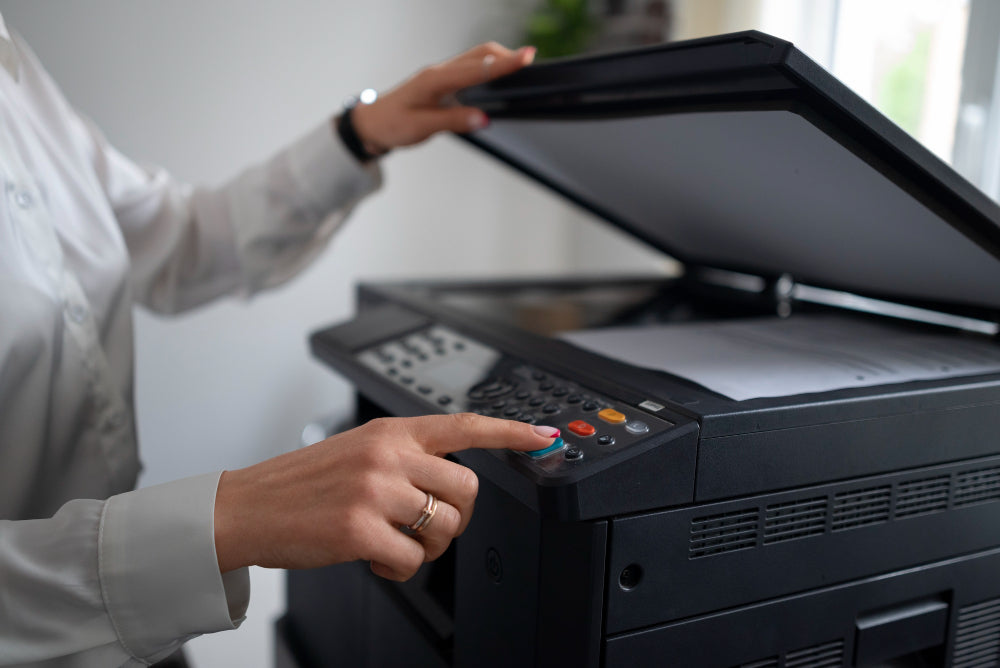 A woman pressing a button on a photocopier or printer with the lid open, preparing to scan or copy documents.