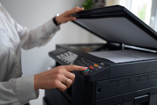 A woman pressing a button on a photocopier or printer with the lid open, preparing to scan or copy documents.
