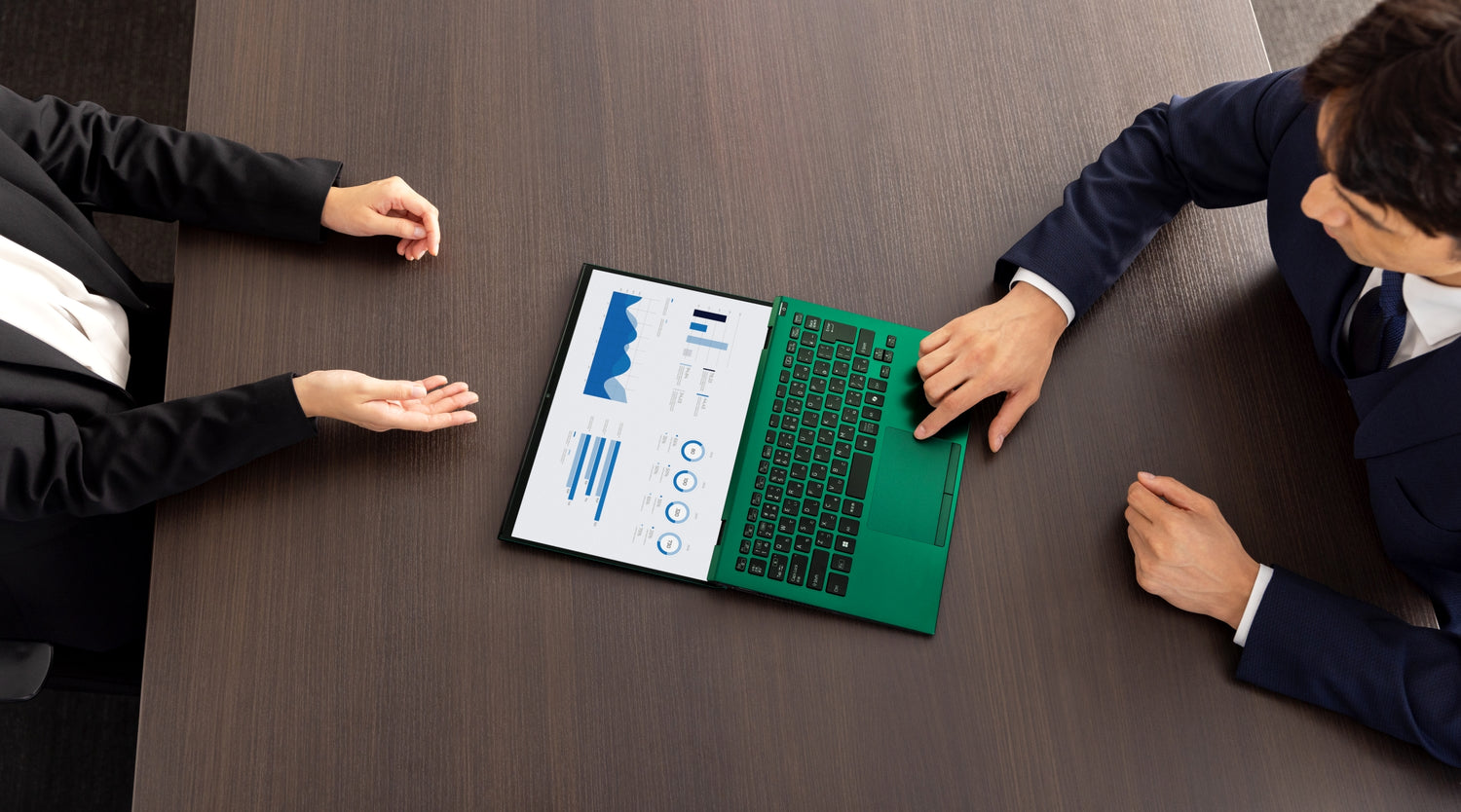 Two professionals discussing data on a laptop displaying graphs during a meeting.