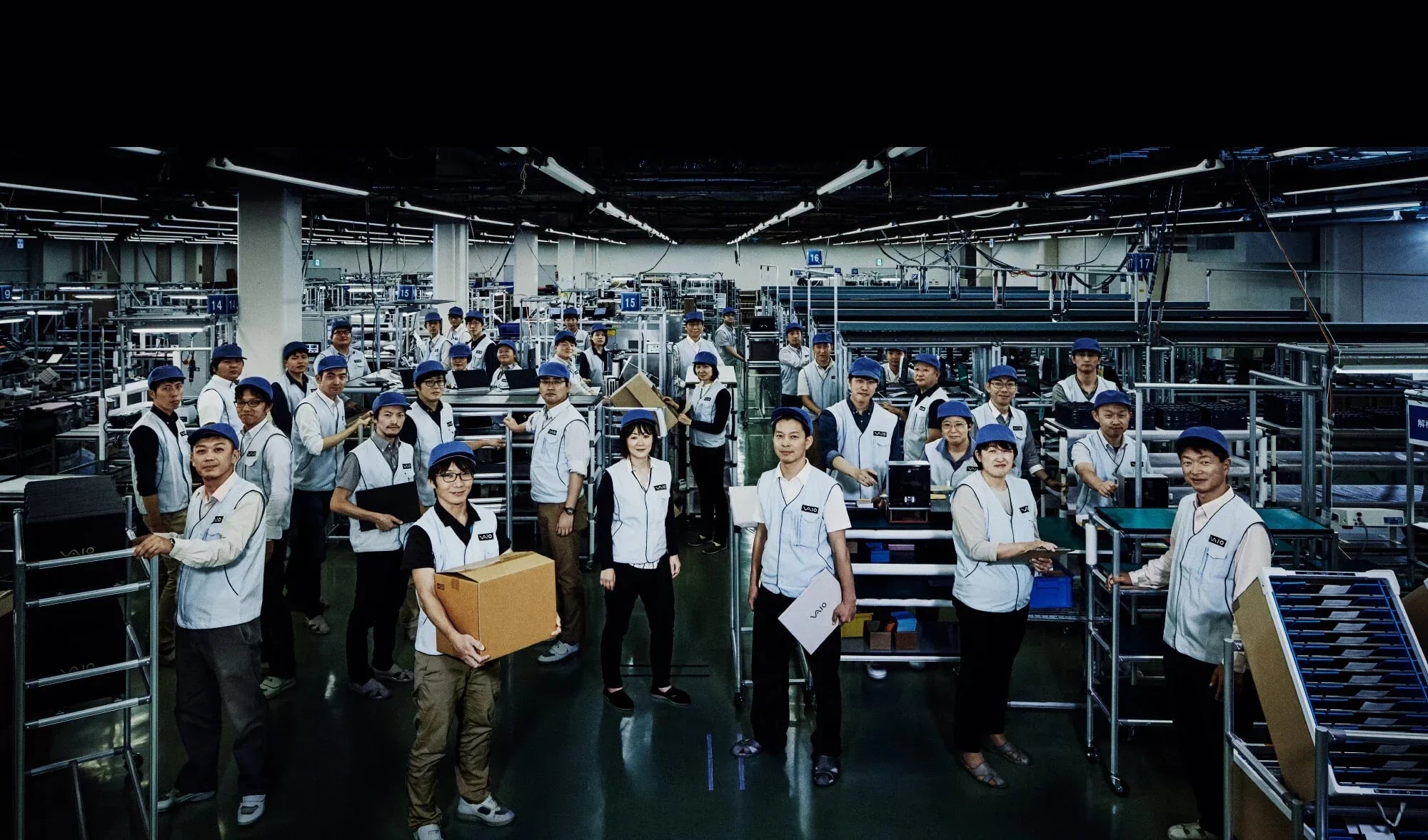 Factory workers in uniforms standing in an organized manufacturing facility, engaged in various tasks and operations.