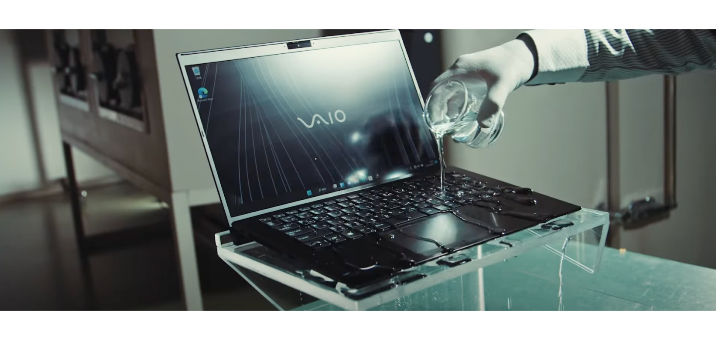 Person pours water on VAIO laptop keyboard, showcasing its water-resistant feature in a controlled test environment.