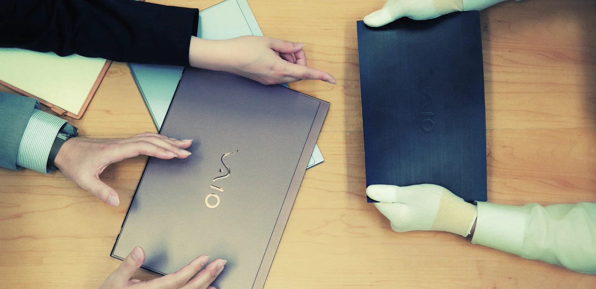 Three pairs of hands handling Vaio laptops on a wooden table; one pair wears gloves.