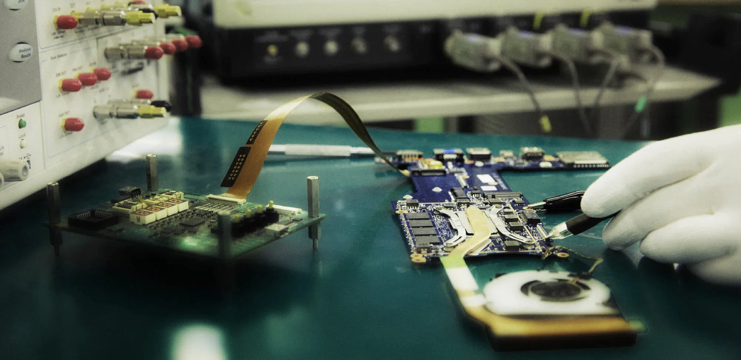 Technician in gloves working on a circuit board with precision tools in an electronics lab, testing components.