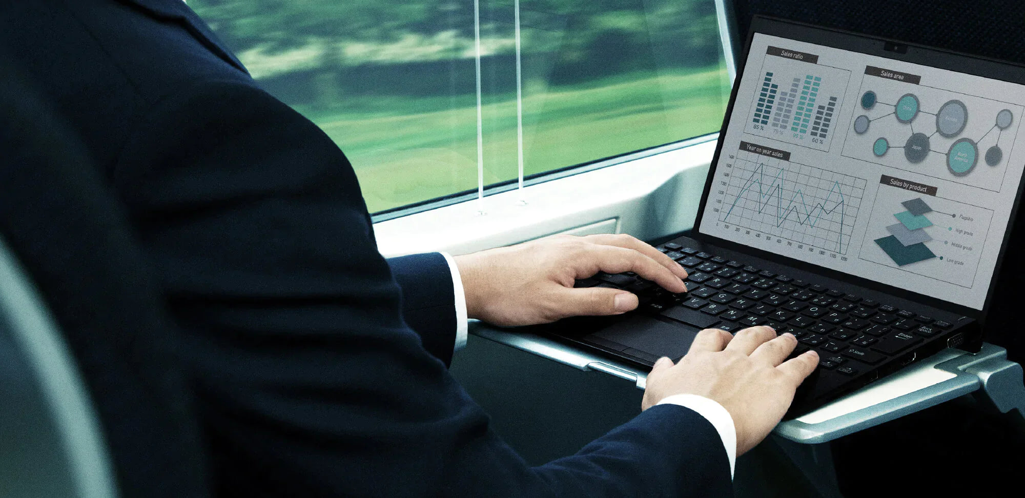 Businessman working on a laptop displaying charts and graphs while traveling on a train with a scenic view outside the window.
