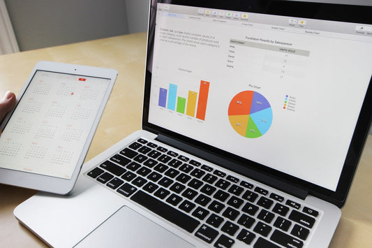 A tablet showing a calendar and a laptop displaying a pie chart and bar graph on a desk.