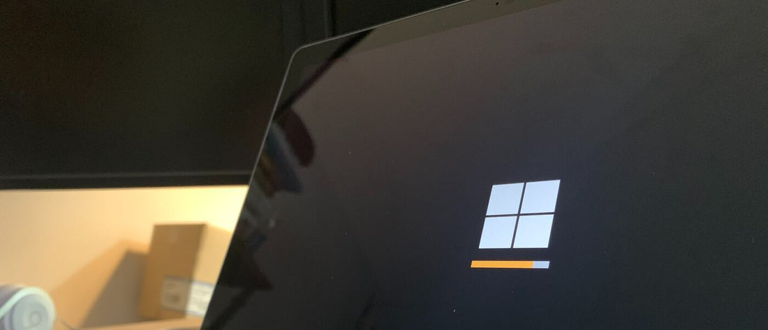 A laptop screen with a Windows logo during an update process, with an orange loading bar at the bottom.