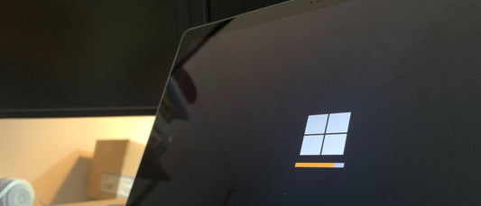 A laptop screen with a Windows logo during an update process, with an orange loading bar at the bottom.