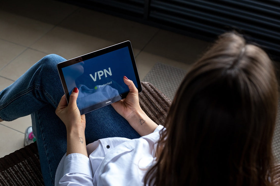 Person holding a tablet displaying a VPN logo on the screen while sitting on a sofa.