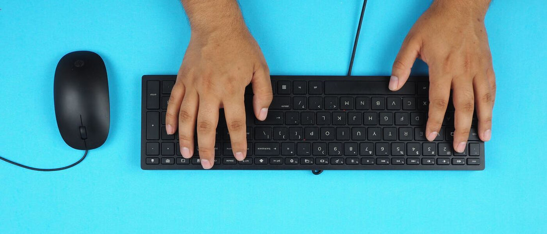 a pair of hands typing on a keyboard, with a computer mouse placed nearby on a blue background.